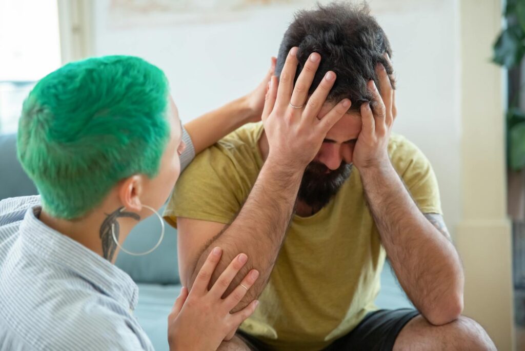 A woman with green hair offering emotional support to a distressed man indoors.