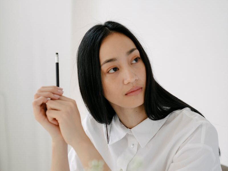 Thoughtful young woman looking away while studying at a desk in a minimalist setting.