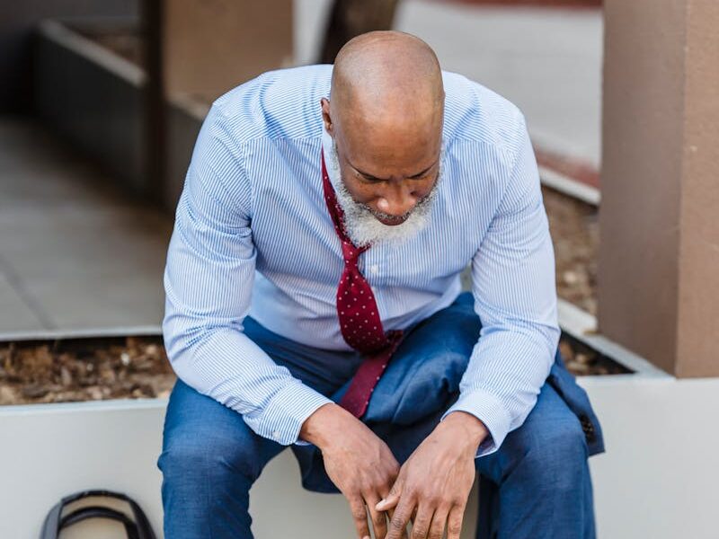 Businessman in distress sitting outdoors with briefcase, reflecting on challenges.