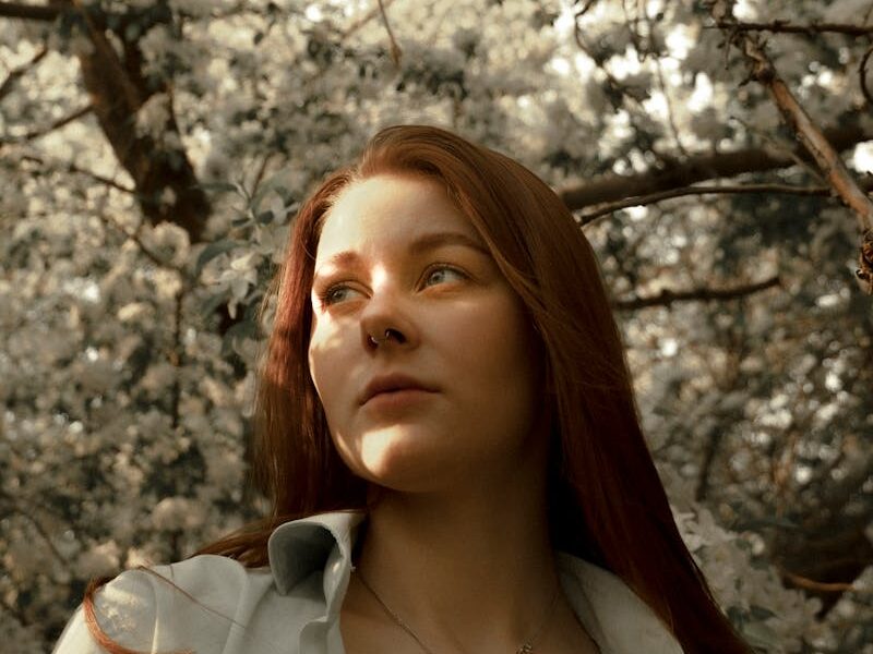 A reflective woman surrounded by blooming white flowers on a sunny spring day.