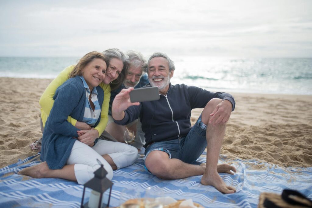 A joyful group of senior friends taking a selfie during a beach picnic by the ocean.