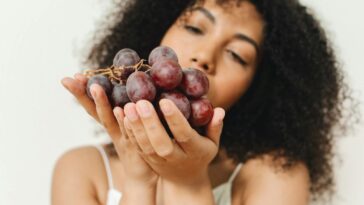 Close-up of a woman holding a bunch of grapes, indoors with soft focus.