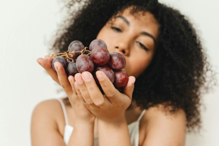 Close-up of a woman holding a bunch of grapes, indoors with soft focus.
