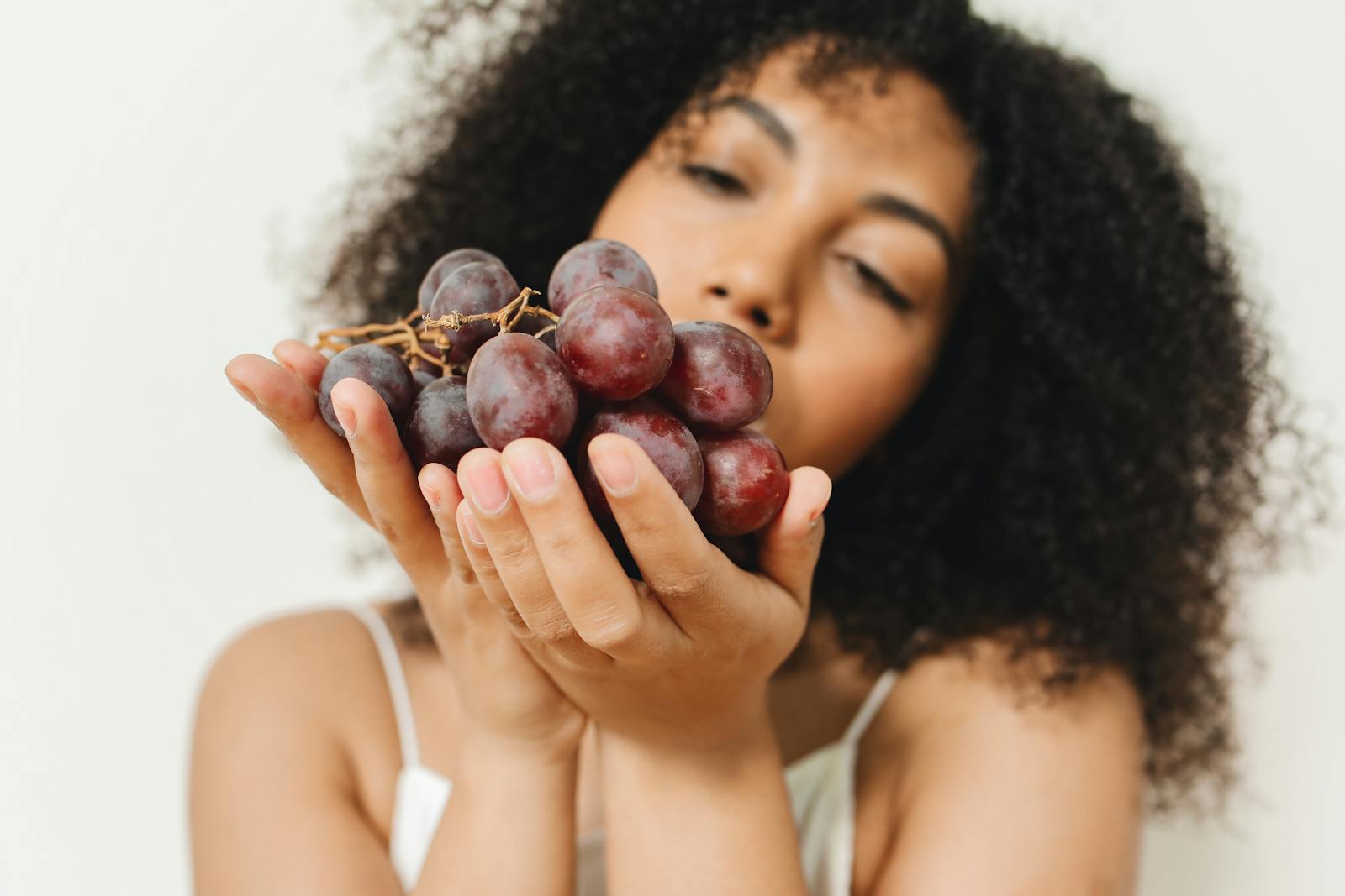 Close-up of a woman holding a bunch of grapes, indoors with soft focus.