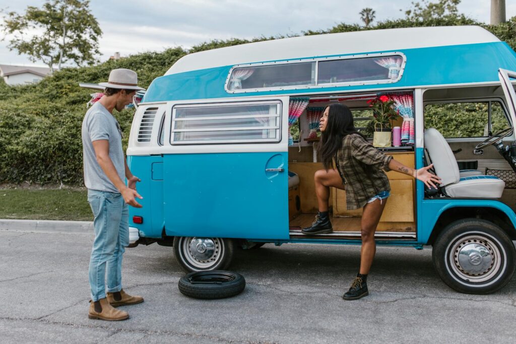 A couple is seen arguing near a vintage campervan with a flat tire on a city street.