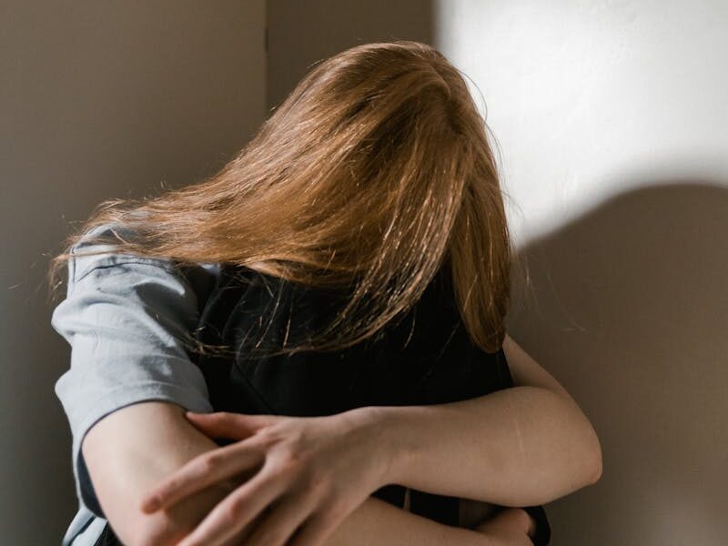 A woman sits alone in a corner, reflecting anxiety and solitude. Soft lighting accentuates her posture.