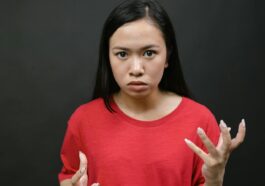 A young woman with expressive hands showing emotions against a dark background.