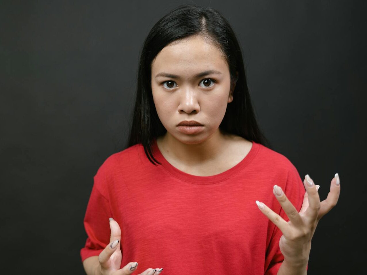 A young woman with expressive hands showing emotions against a dark background.