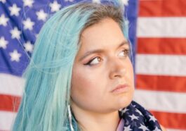 Close-up of a woman with blue hair holding an American flag, expressing patriotism.