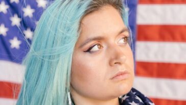 Close-up of a woman with blue hair holding an American flag, expressing patriotism.