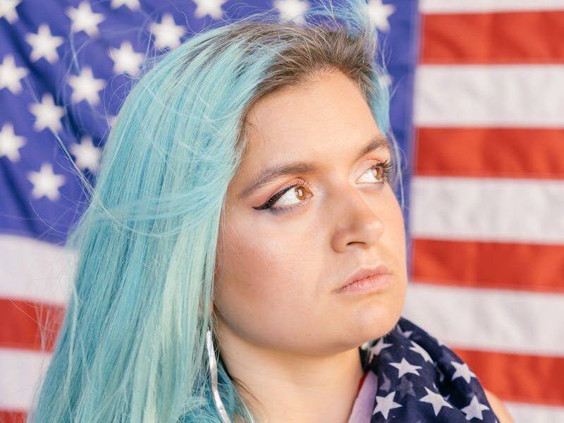 Close-up of a woman with blue hair holding an American flag, expressing patriotism.