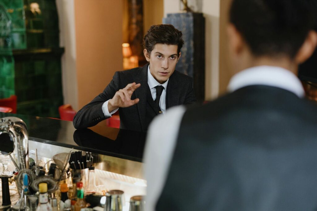 A classy interaction between a gentleman and a waiter at a stylish vintage bar setting.