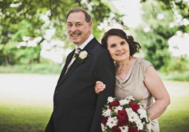 man in black suit standing beside woman in gray sleeveless dress holding bouquet of flowers