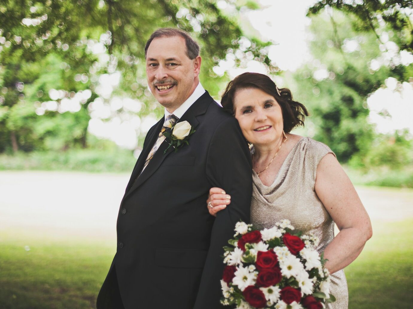 man in black suit standing beside woman in gray sleeveless dress holding bouquet of flowers