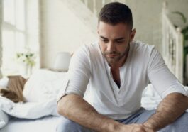 Man sitting on bed looking down thoughtfully.