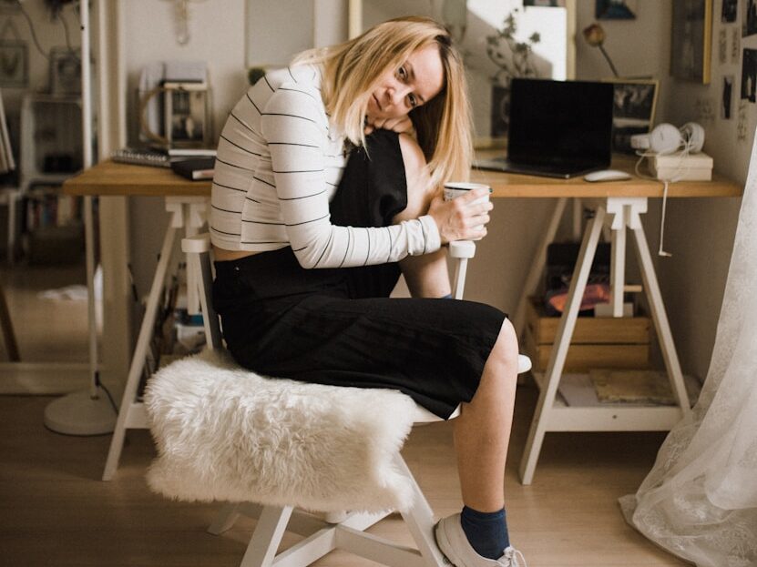 woman sitting on stool resting her head on her knee inside room
