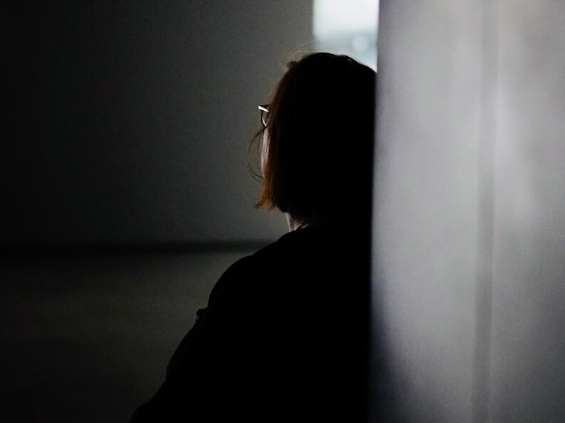 a woman sitting in a dark room next to a wall