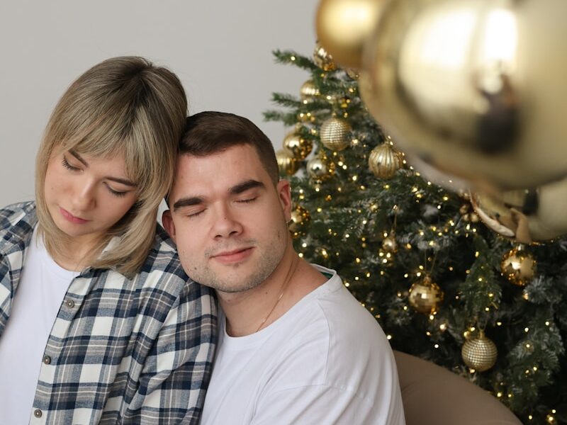 A man and woman sitting next to a christmas tree