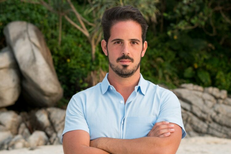 A man standing with his arms crossed on a beach