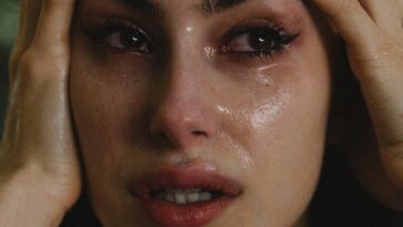 A woman crying with hands on her head.