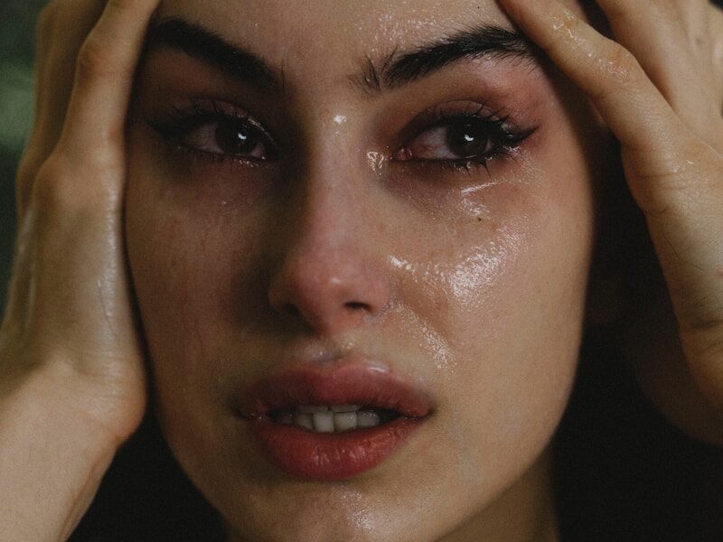 A woman crying with hands on her head.
