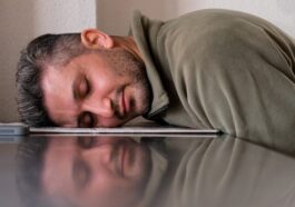 A man is sleeping on the floor with his head on a laptop