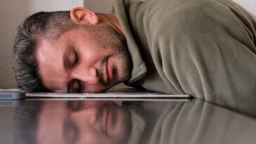 A man is sleeping on the floor with his head on a laptop