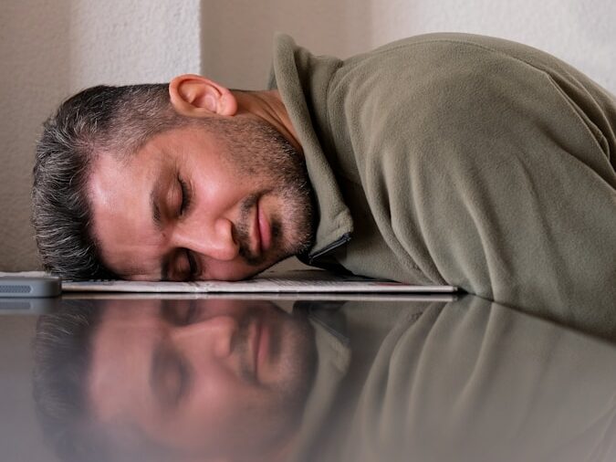 A man is sleeping on the floor with his head on a laptop