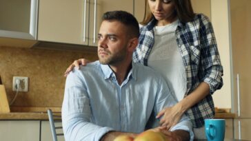 Woman comforts man at kitchen table with food.