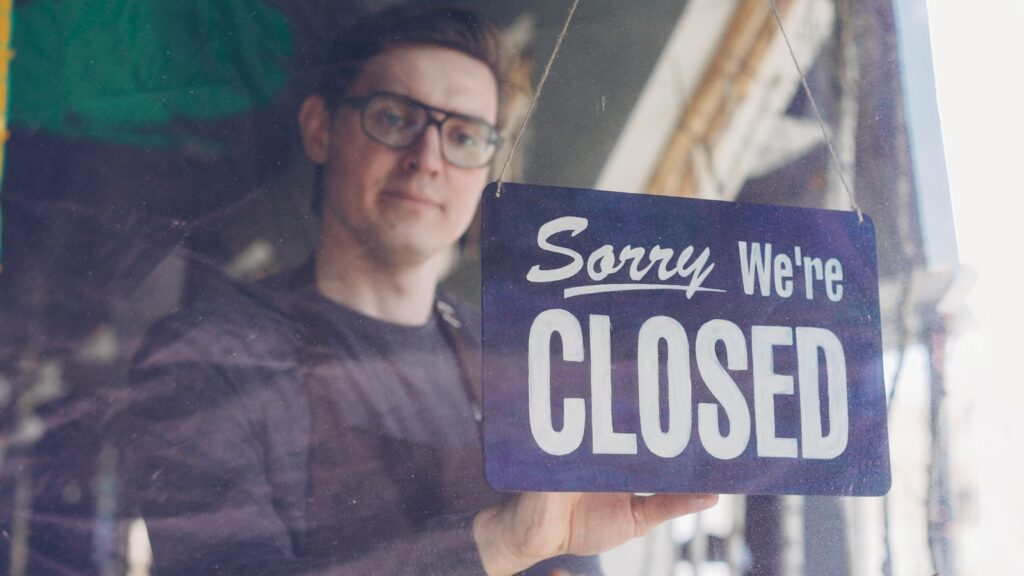 A man shows a "sorry, we're closed" sign.