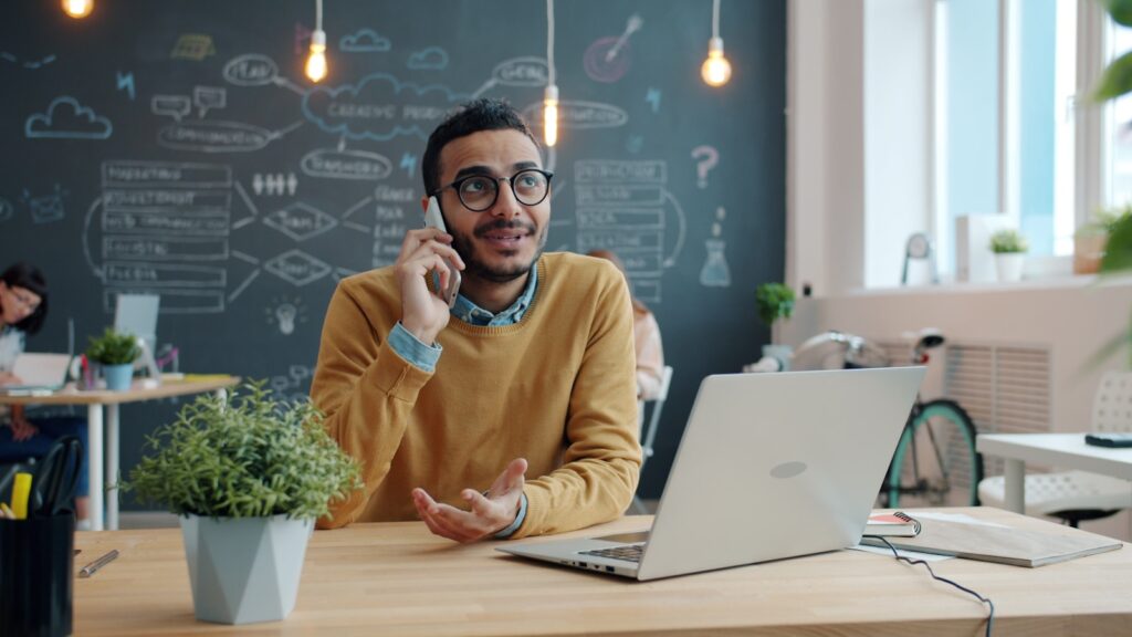 Man talking on phone at desk with laptop.