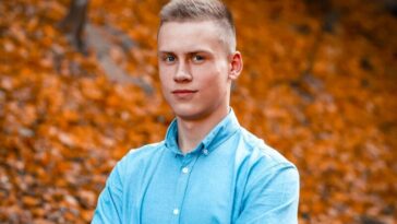 man in blue dress shirt standing on brown leaves during daytime