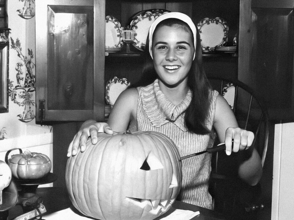 a black and white photo of a woman carving a pumpkin