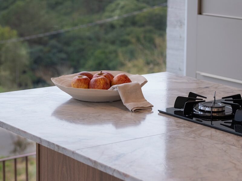 Bowl of apples on marble countertop with stove.