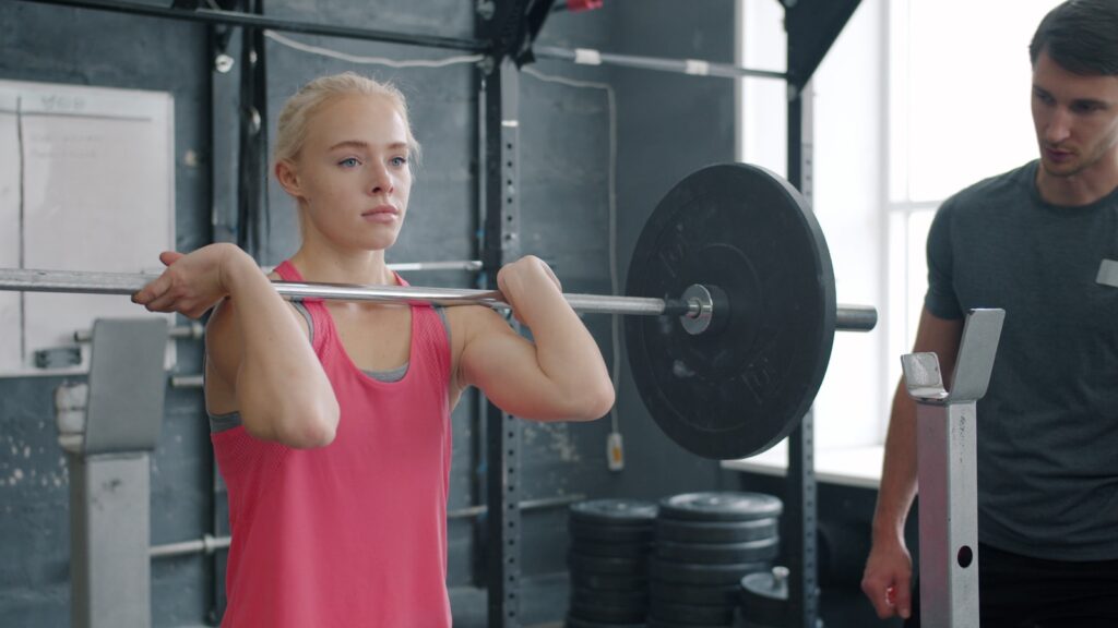 Woman lifting barbell with trainer watching