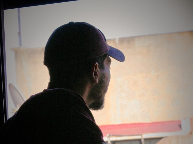 a man sitting in front of a window with a hat on