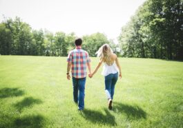 man and woman walking on green grass field surrounded with trees