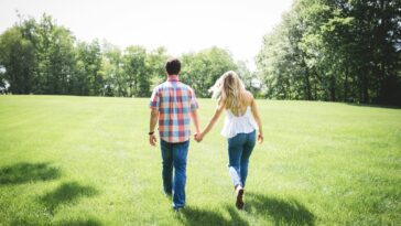 man and woman walking on green grass field surrounded with trees