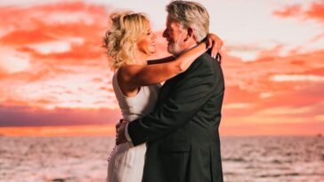 a bride and groom embracing on the beach at sunset