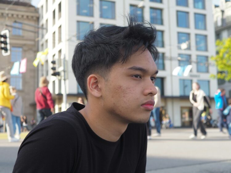 A young man poses outdoors, looking contemplative.
