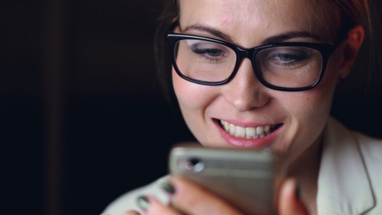 Woman wearing glasses smiles at her smartphone