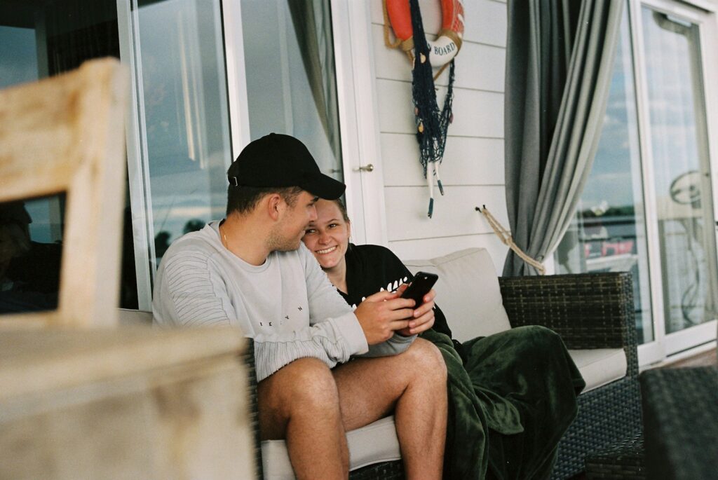 a man and woman sitting on a bench looking at their phones