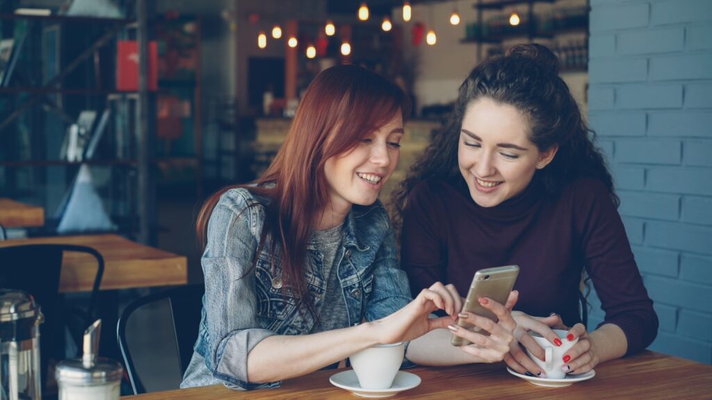 Two friends smile while looking at a phone.