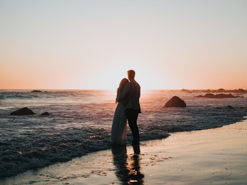 silhouette photo of couple standing on beach watching sunset