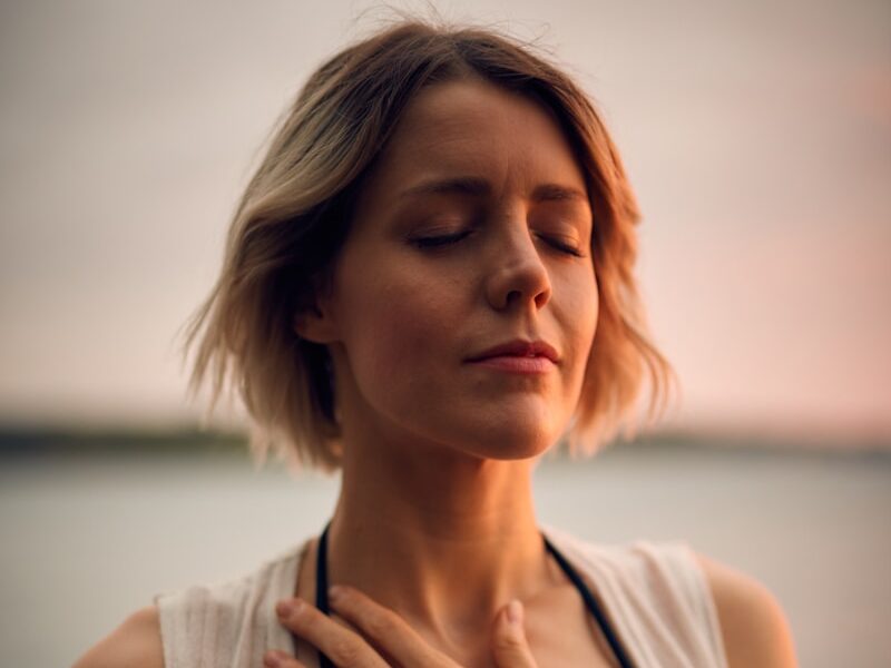 woman in white vest and black bikini with hand on chest