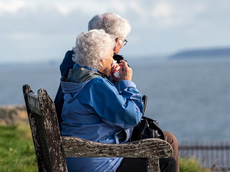 man and woman sitting on gray wooden bench viewing blue sea during daytime