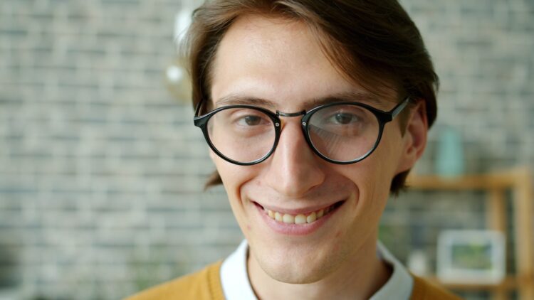 Young man with glasses smiles warmly at the camera