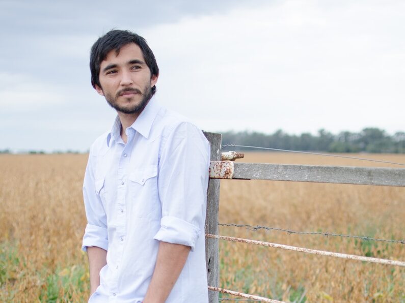a man leaning against a fence in a field