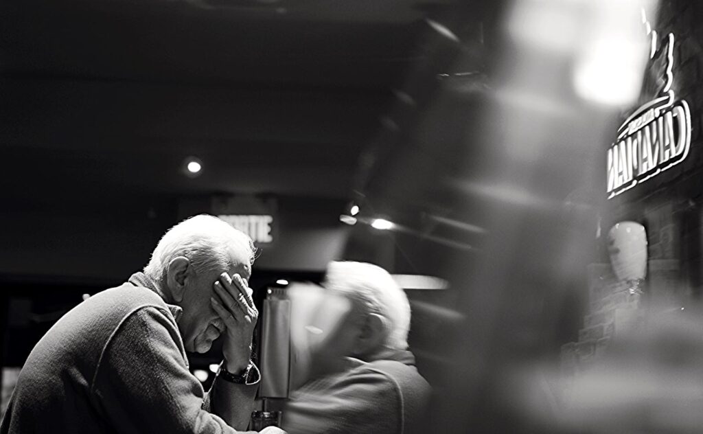 Black and white image of an elderly man reflecting in a café setting.