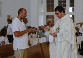 Priest distributing communion during a Catholic mass with congregation present.